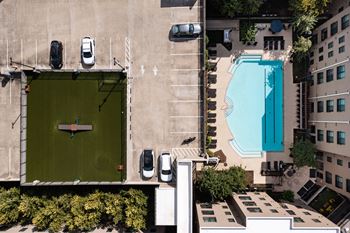 A swimming pool is surrounded by a parking lot and a building.